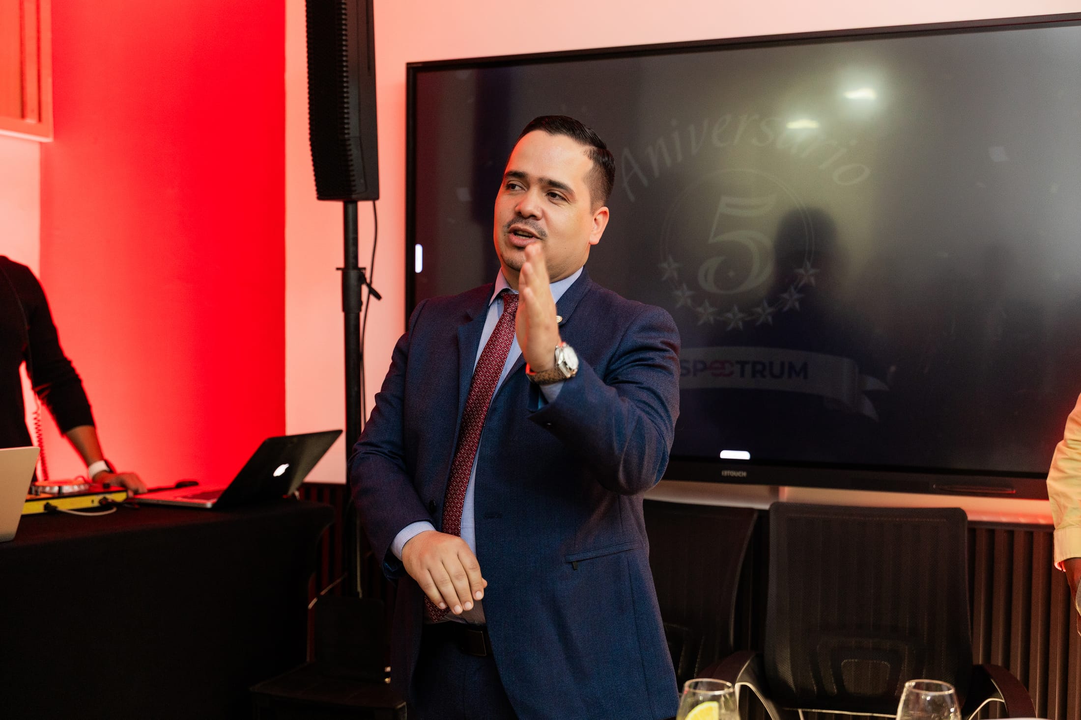 Edison Hernandez, director comercial de Spectrum, habla frente a una pantalla con el logo del quinto aniversario